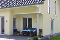 Massivhaus Putzbau in Ibbenbüren, NRW, Freisitz Terrasse, hochgezogener Eingangsbereich Glas, Schornstein, Pfettenköpfe